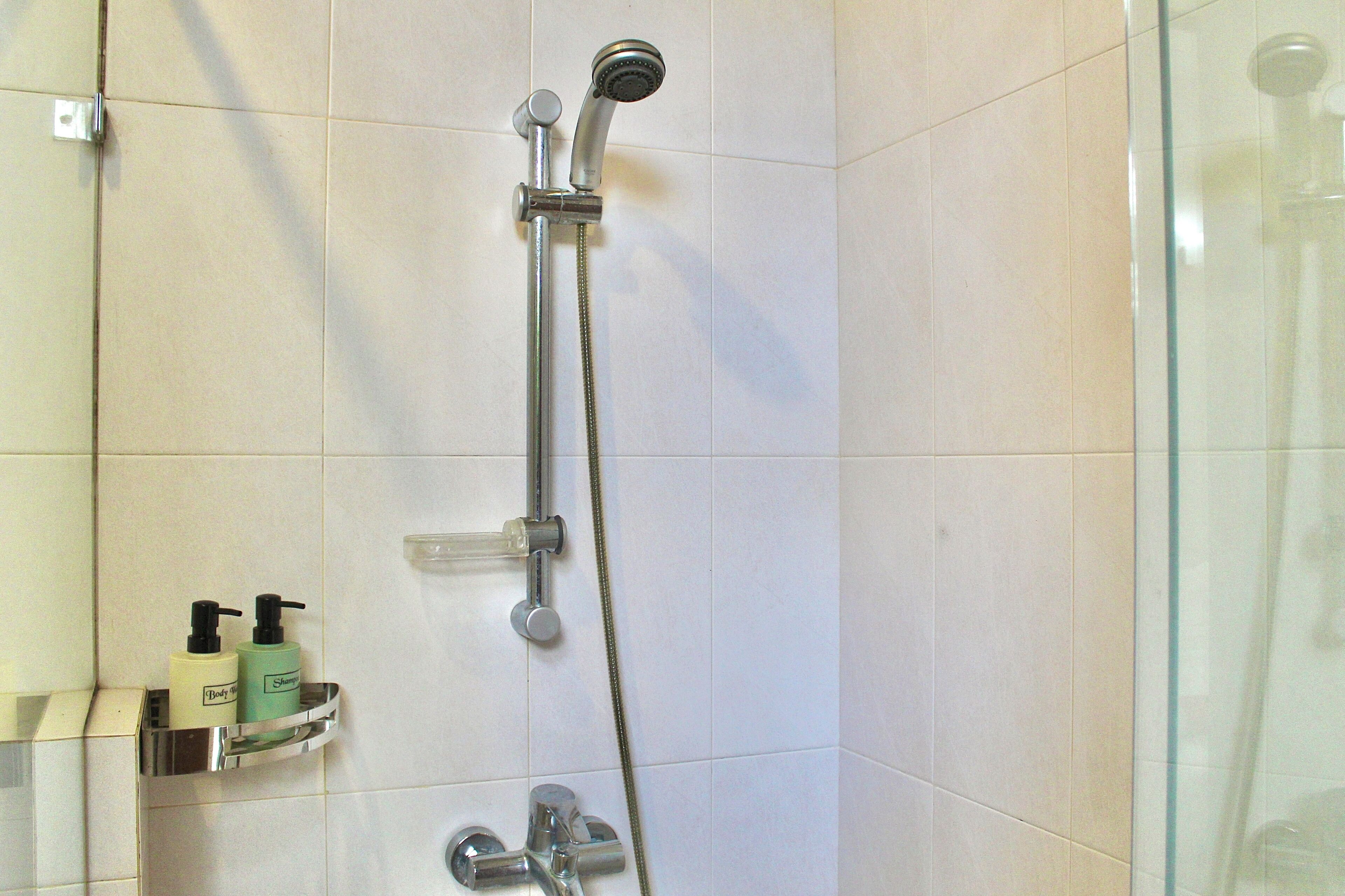 Ducha con cabezal de ducha de mano y grifo empotrado en la pared. Abajo, en un estante, hay dos botellas de champú y gel de baño.