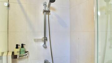 Ducha con cabezal de ducha de mano y grifo empotrado en la pared. Abajo, en un estante, hay dos botellas de champú y gel de baño.