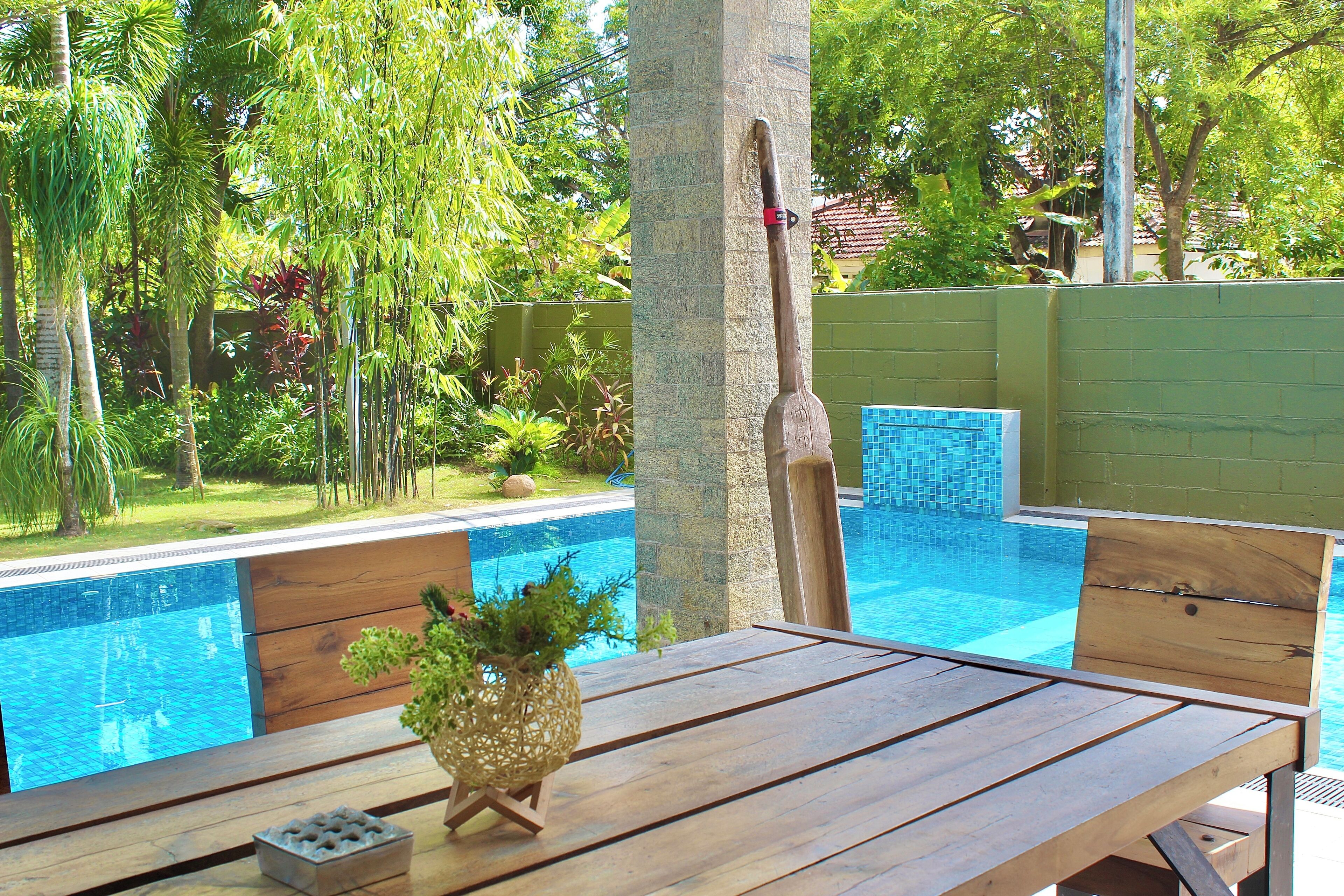 Mesa de madeira com uma planta e um pequeno recipiente, com vista para uma piscina com borda revestida de azulejos.
