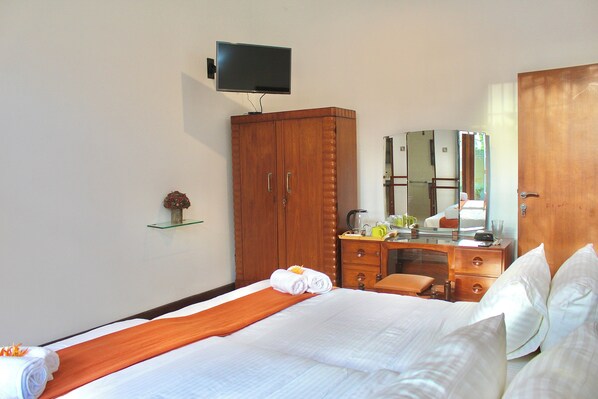 A hotel room with a bed, a wooden wardrobe, a desk with a mirror, and a television mounted on the wall. - Tropical Terrace Negombo (Negombo)