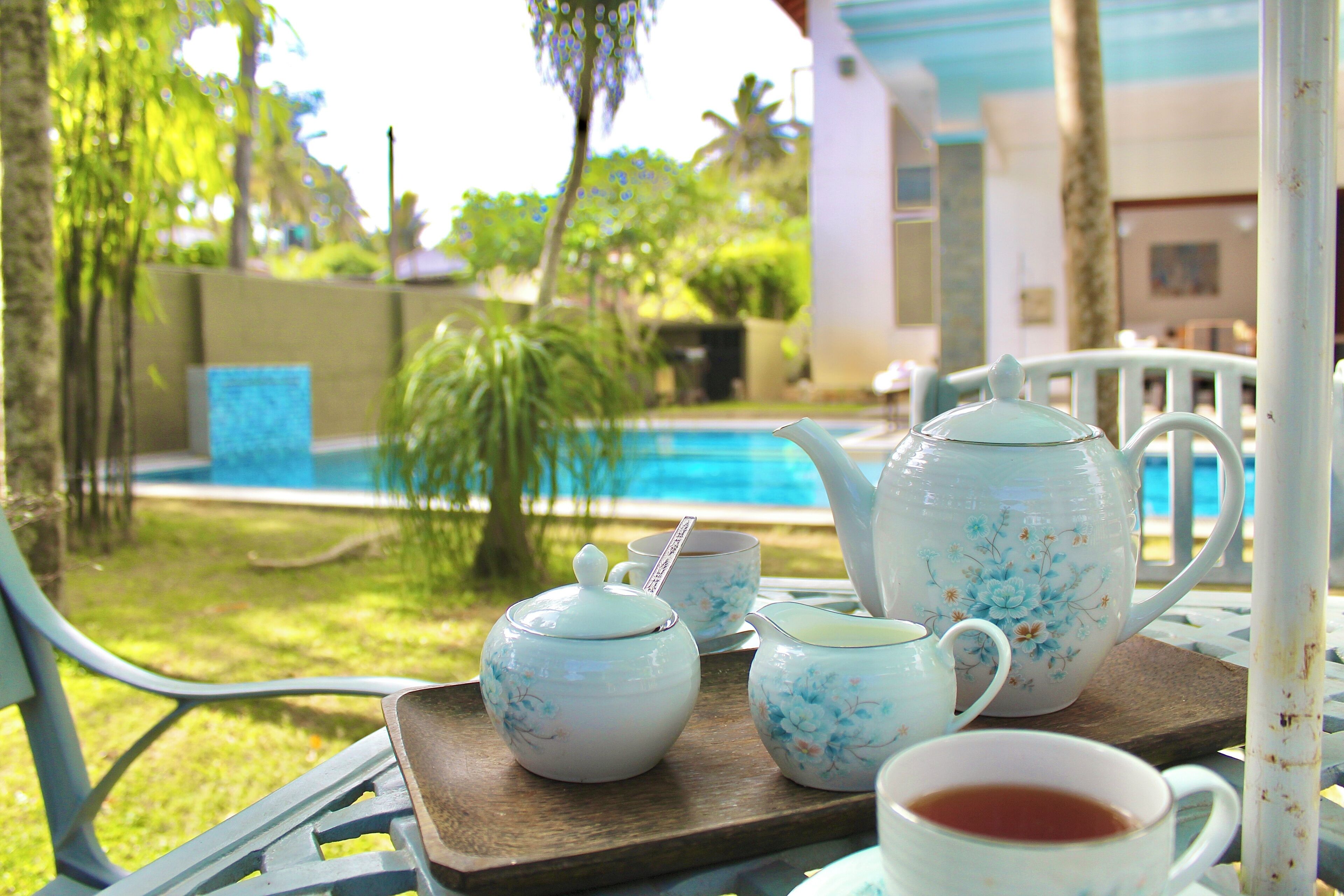 A table with a tray holding a teapot, cups, and a teacup, set against a poolside view.