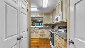A kitchen with white cabinetry, a wooden floor, a built-in oven, and a microwave. - The Lady Bug on Lake Martin (Our Town)
