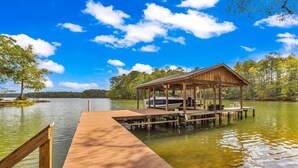 A wooden dock extending into a lake with a covered seating area and a boat docked nearby. - The Lady Bug on Lake Martin (Our Town)