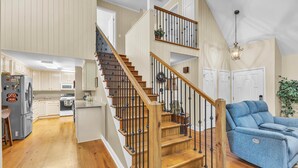 A spacious living area with a wooden staircase, a blue sofa, and a kitchen with white cabinets. - The Lady Bug on Lake Martin (Our Town)