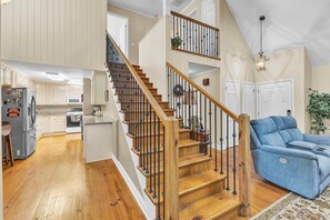 A spacious living area with a wooden staircase, a blue sofa, and a kitchen with white cabinets.