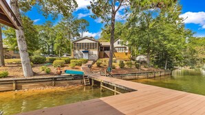 A lakeside property with a dock, wooden deck, and a house with a large window overlooking the water. - The Lady Bug on Lake Martin (Our Town)