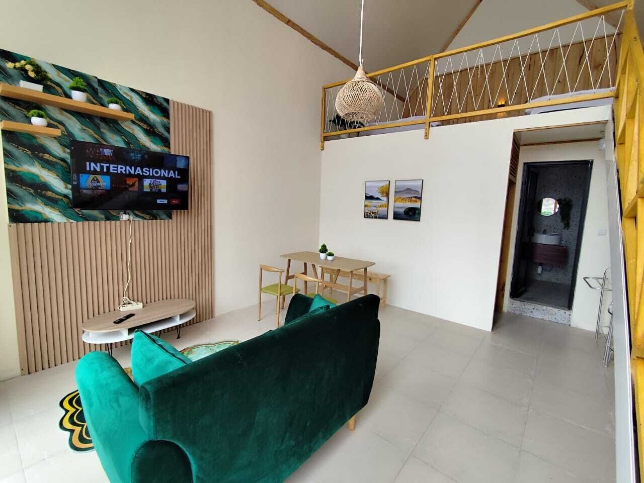 Ein modernes Wohnzimmer mit einem grünen Sofa, einem an einer Holzwand montierten Fernseher, einem Esstisch mit Stühlen und einer Treppe, die zu einer oberen Ebene führt.