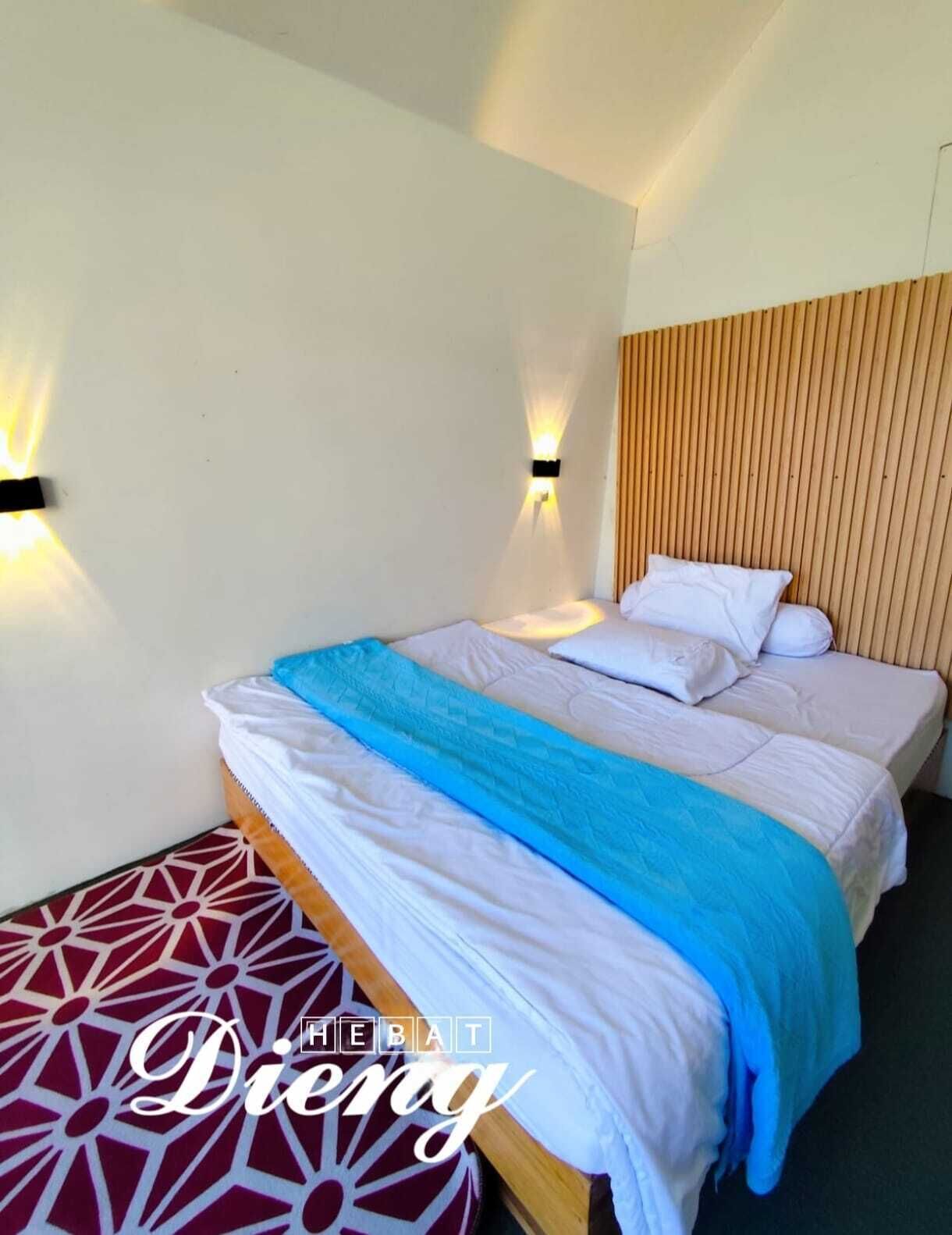 A hotel room with a bed, two wall-mounted lights, a wooden headboard, and a patterned floor.