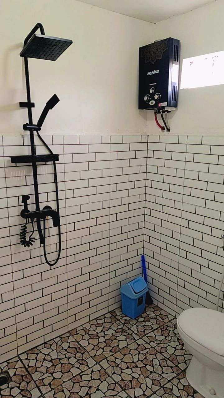 A bathroom with a shower, a toilet, and a blue trash bin.