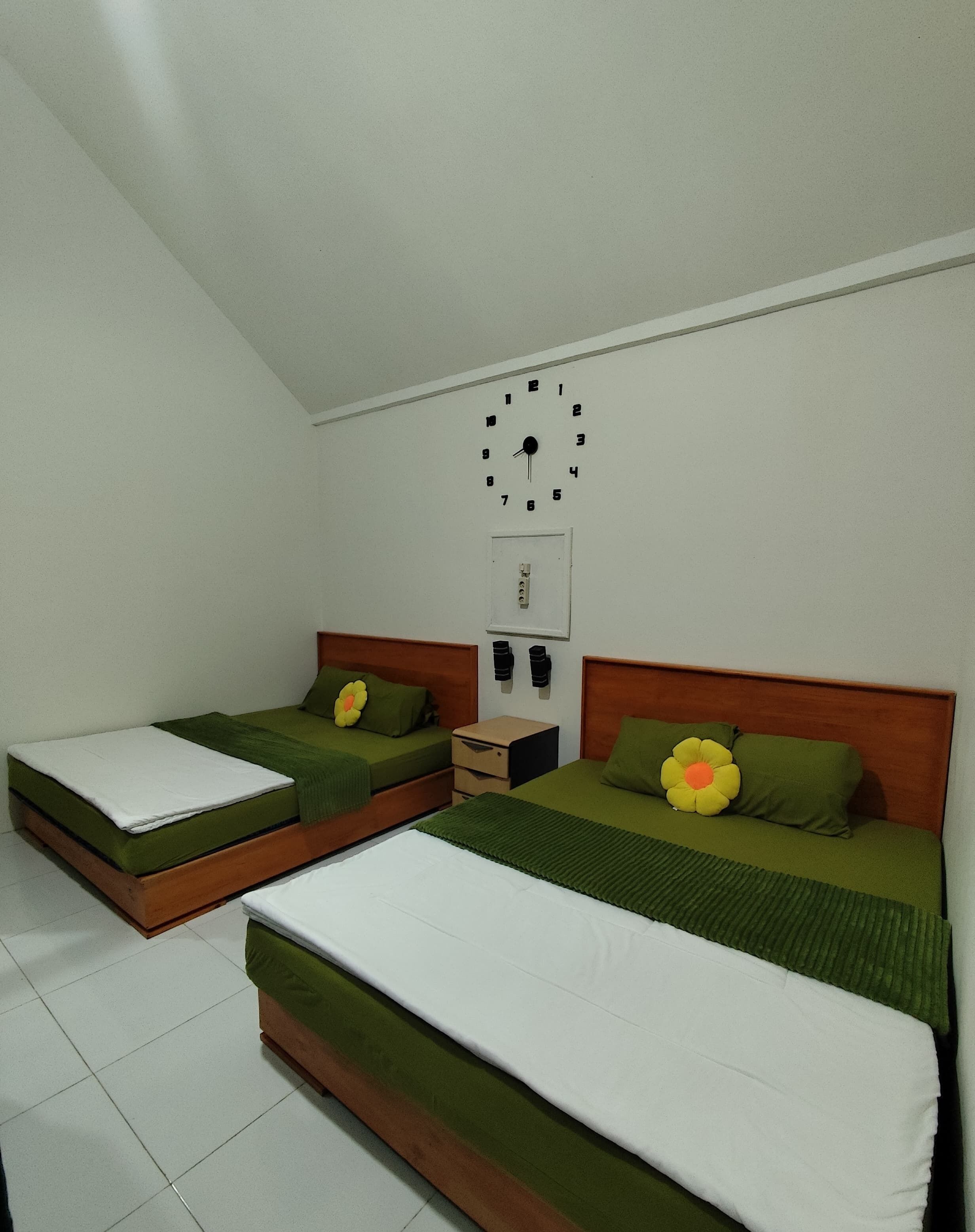 A bedroom with two single beds, a wall clock, and a small bedside table with a lamp.