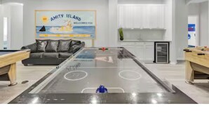 Uma sala de estar espaçosa com mesa de bilhar, sofá e cozinha ao fundo.
