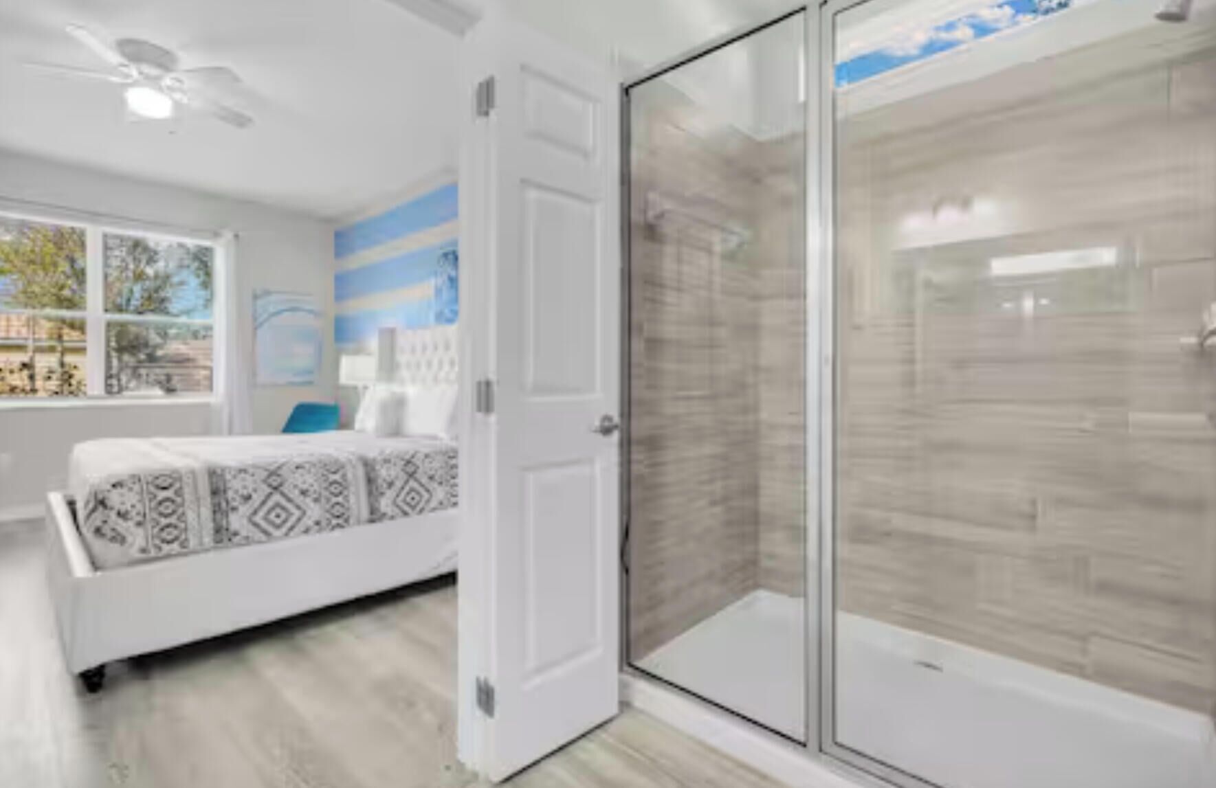 A modern bedroom with a bed, a glass shower enclosure, and a view of the outdoors.