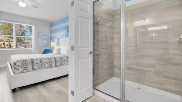 Quarto moderno com cama, chuveiro de vidro e vista para o exterior.