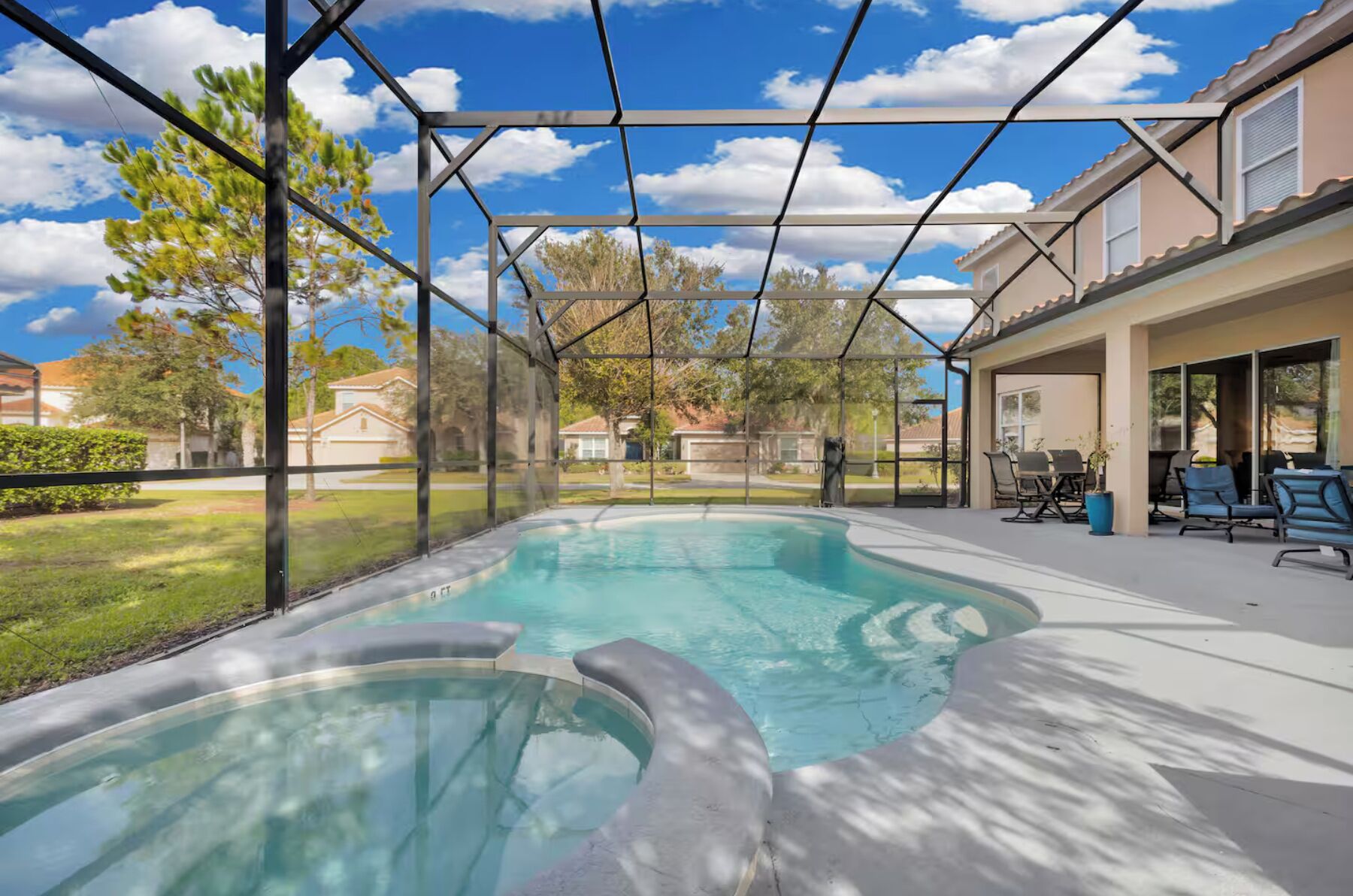 Una piscina con cerramiento de vidrio, rodeada por un patio con mobiliario exterior.