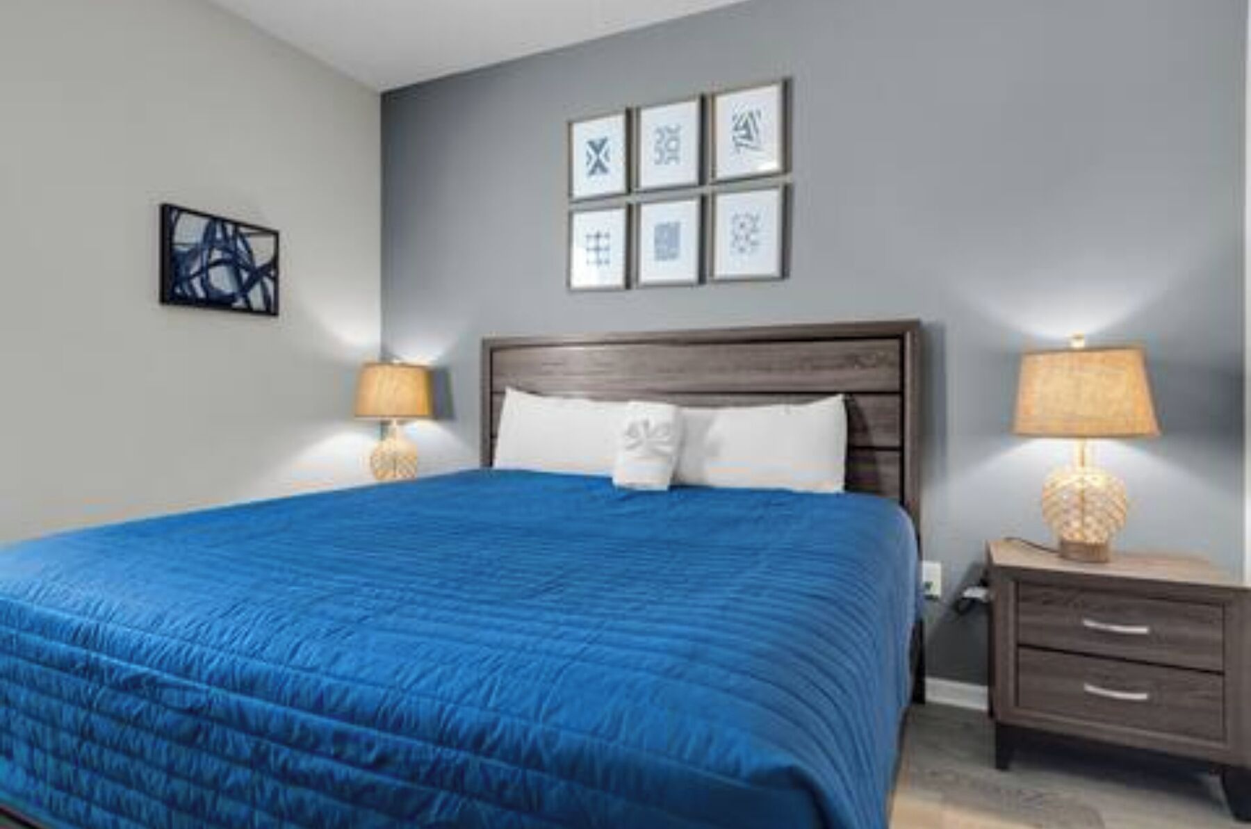 Un lit bien fait, avec une couvre-lit bleue, une tête de lit en bois et deux lampes de chevet.