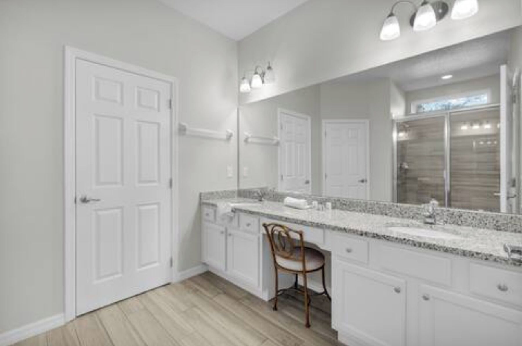 A bathroom with a large mirror, white cabinets, and a wooden chair.