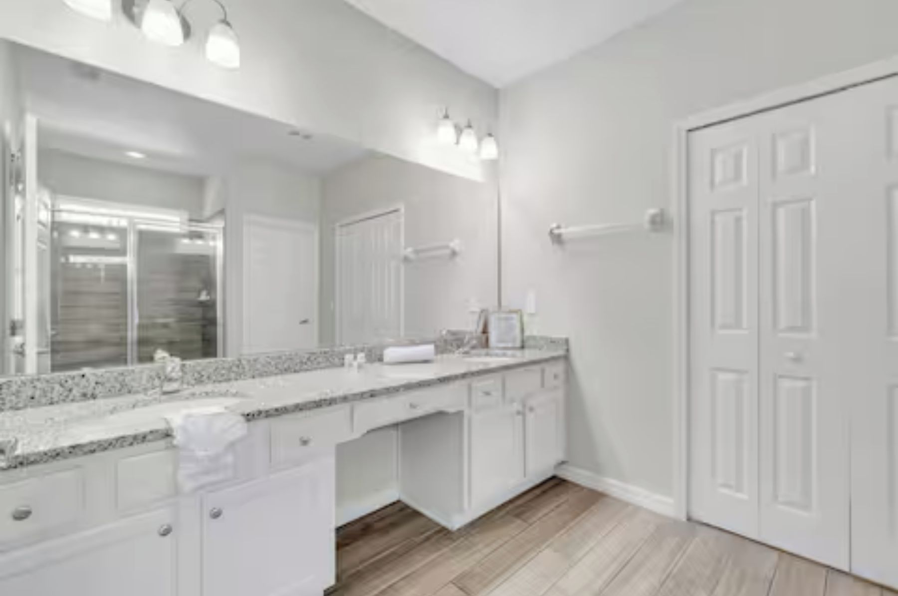 A modern bathroom with a large mirror, white cabinetry, and a wooden floor.