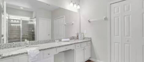 A modern bathroom with a large mirror, white cabinetry, and a wooden floor.
