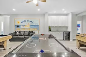 Amplia sala de estar con mesa de billar, sofá y cocina al fondo.