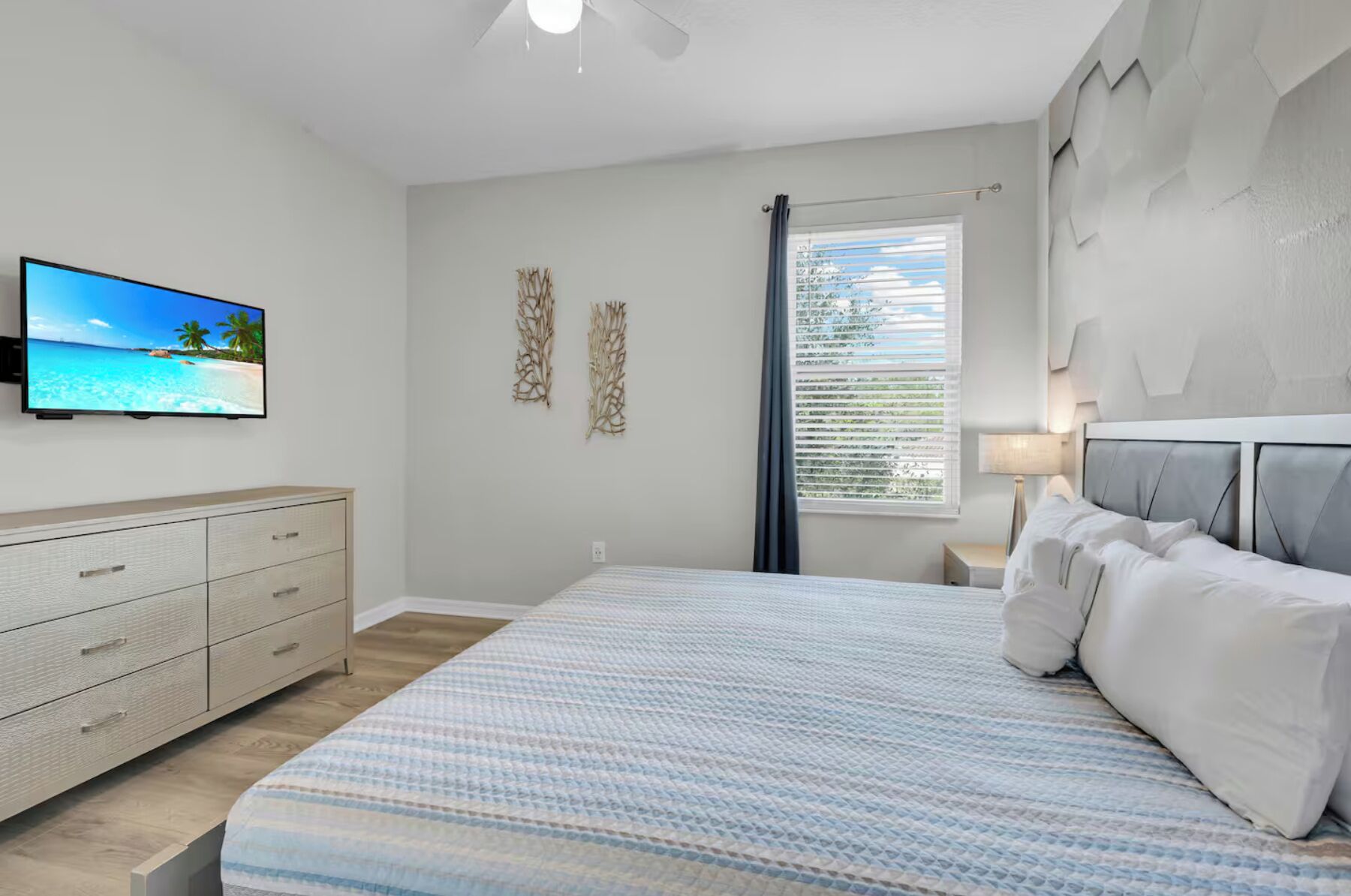 A bedroom with a bed, a TV on the wall, a dresser, and a window with blinds.