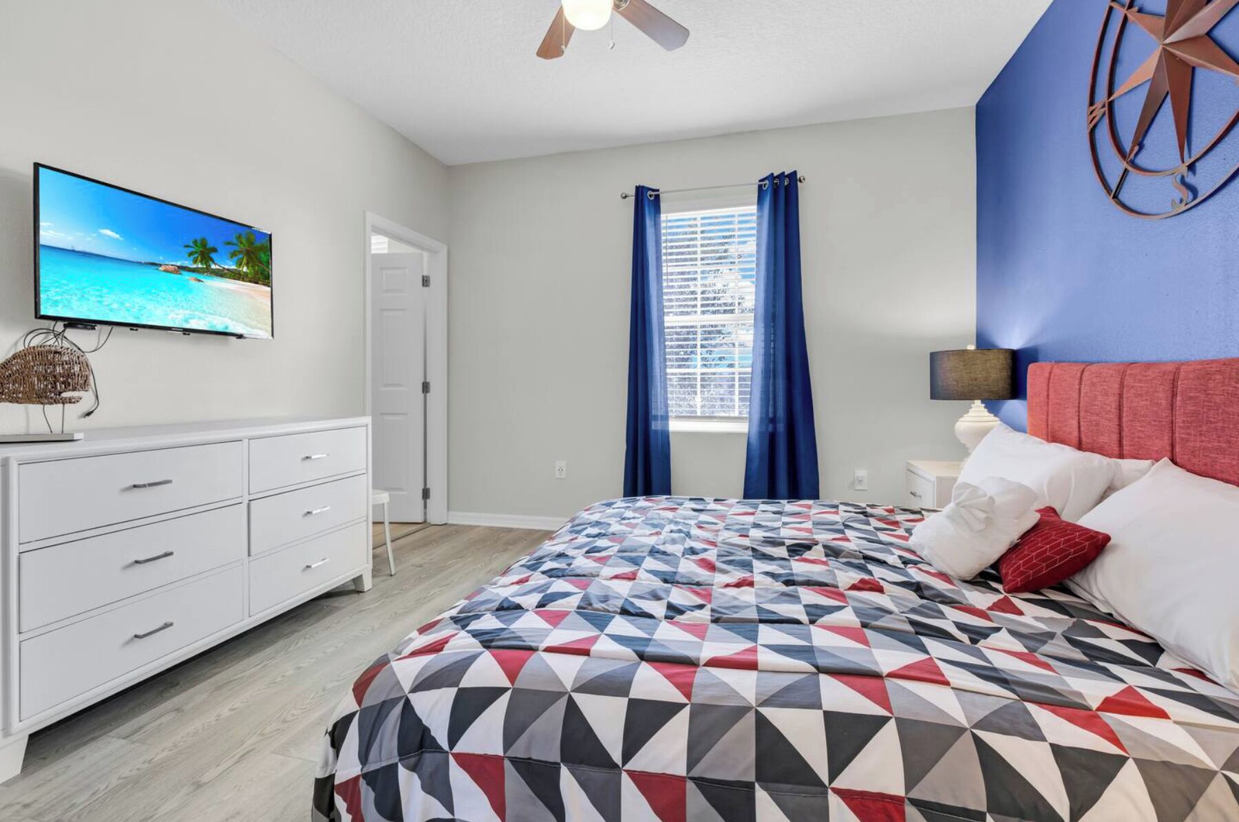 Un dormitorio con cama, televisión, cómoda y ventana con cortinas.