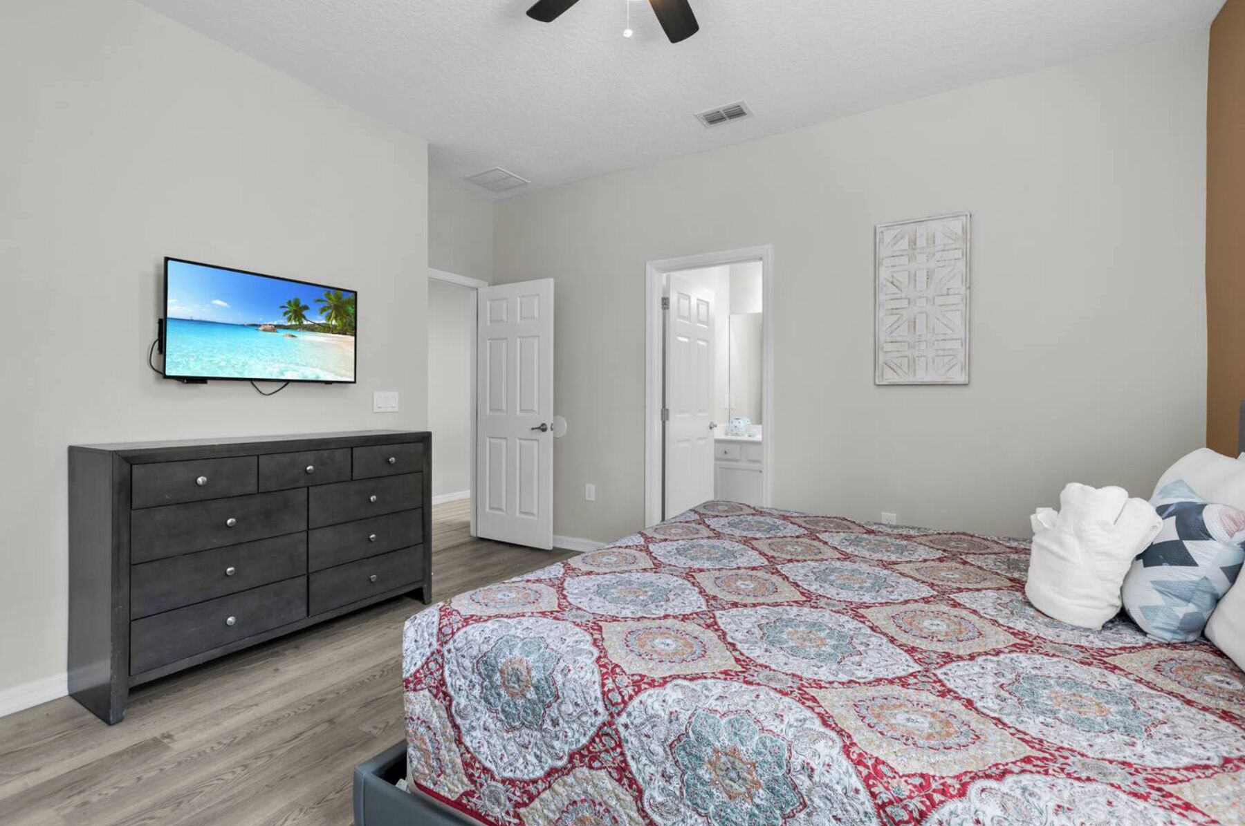 Une chambre à coucher comprenant un lit, une commode, un téléviseur et une porte donnant sur une autre pièce.