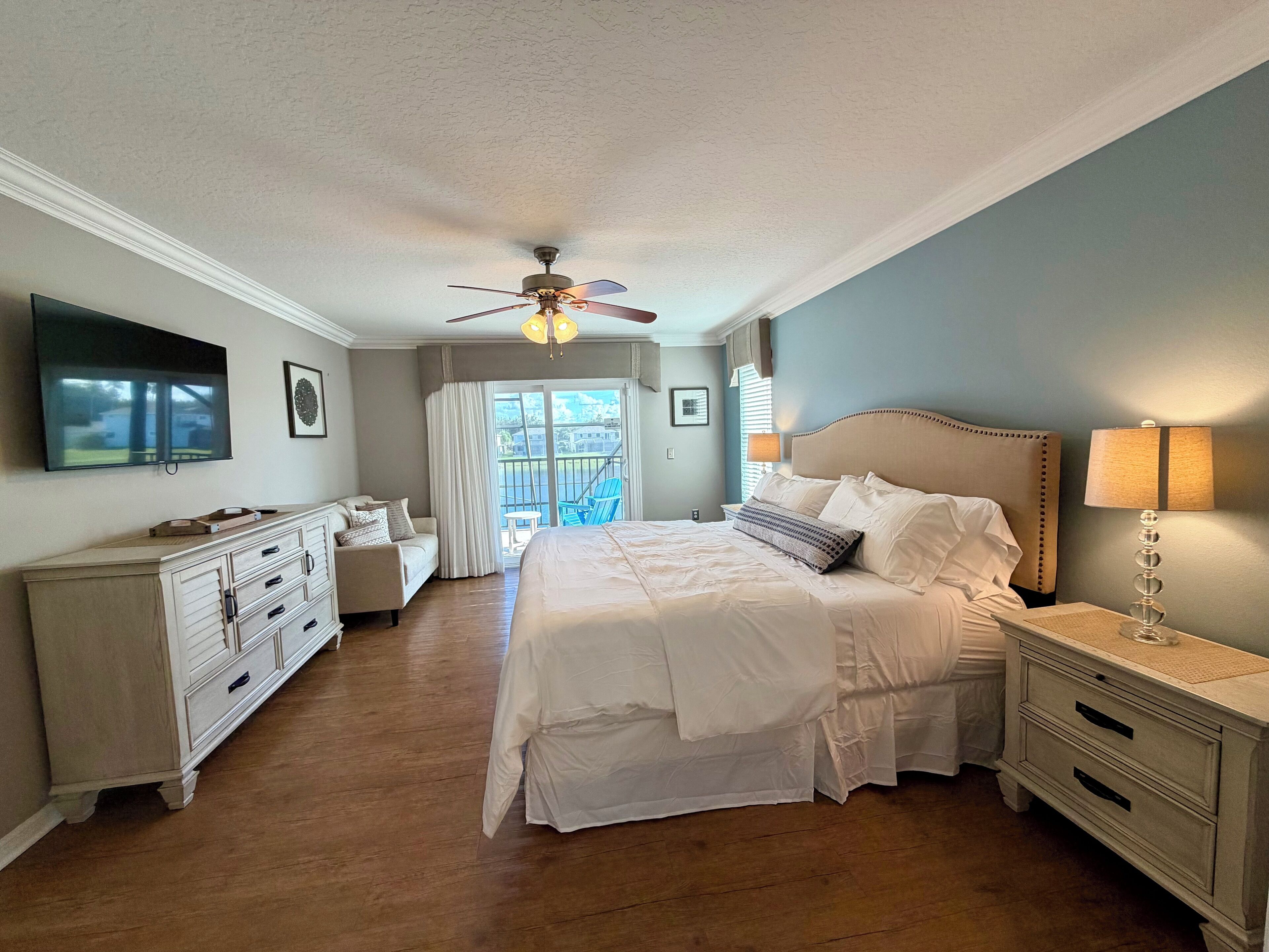 A bedroom with a bed, a ceiling fan, a TV, a dresser, and a window with curtains.