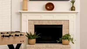Una sala de estar con chimenea, televisor montado y mesa de futbolín.