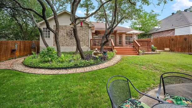 Un patio trasero residencial con una casa, una terraza de madera y un área de patio con sillas.