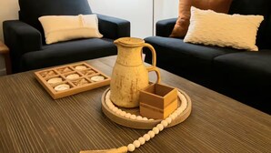 Un salón con dos sofás negros, una mesa de centro de madera y decoración en la pared.