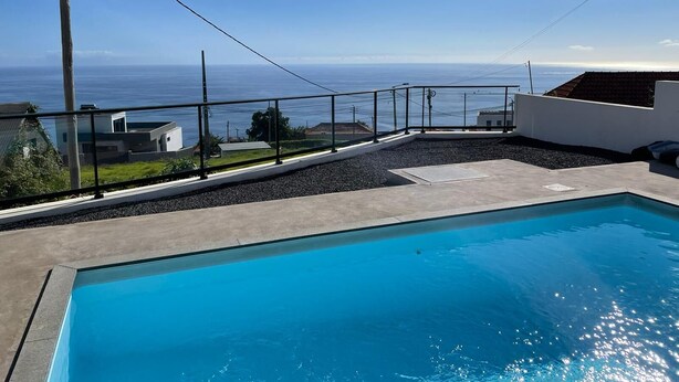 A swimming pool with a view of the ocean, surrounded by a concrete deck and a metal railing.