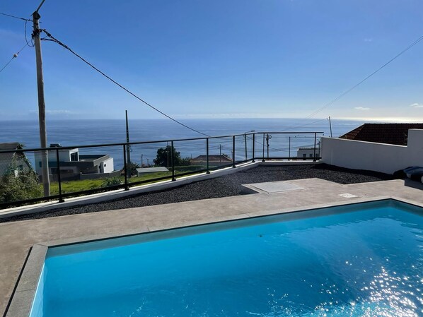 A swimming pool with a view of the ocean, surrounded by a concrete deck and a metal railing.