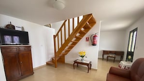 A living room with a wooden staircase, a wooden cabinet, a small table with flowers, and a brown leather sofa.