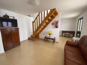 A living room with a wooden staircase, a wooden cabinet, a small table with flowers, and a brown leather sofa.