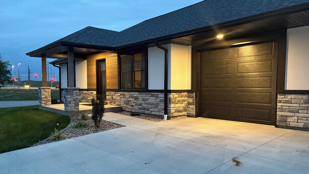 Una casa moderna con fachada de piedra, puerta de garage oscura y entrada bien iluminada.