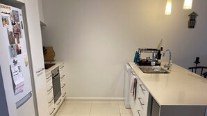A modern kitchen with white cabinetry, a built-in oven, a dishwasher, and a large island with a sink. - Large 3x bedroom apartment directly opposite beach. Very comfortable and cosy. (Coffs Harbour)