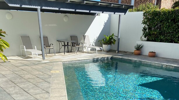 A swimming pool with a metal ladder, surrounded by tiled flooring and potted plants. - Large 3x bedroom apartment directly opposite beach. Very comfortable and cosy. (Coffs Harbour)