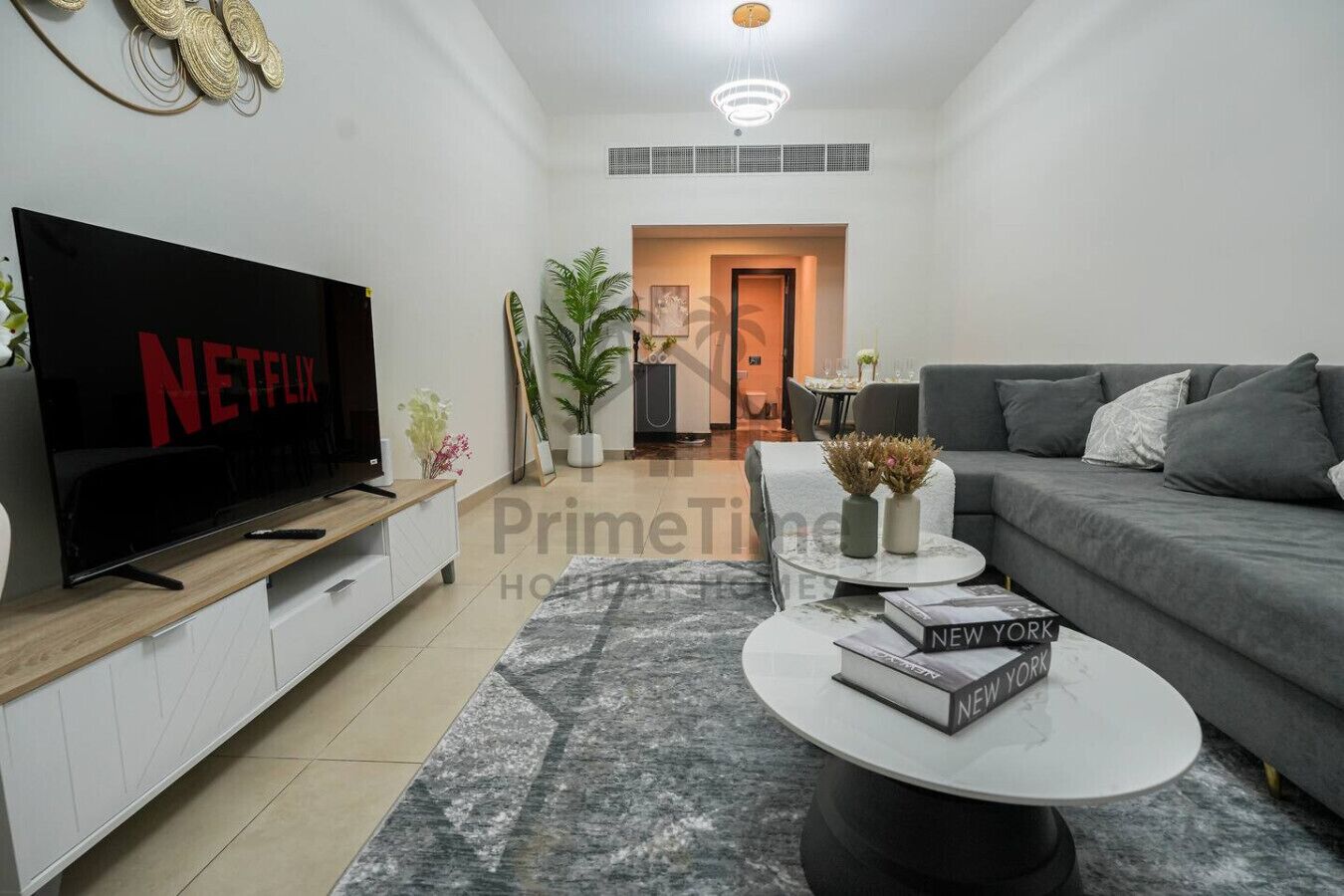 Una sala de estar moderna con un televisor de pantalla plana grande, un sofá gris, una mesa de centro con libros y una alfombra estampada.