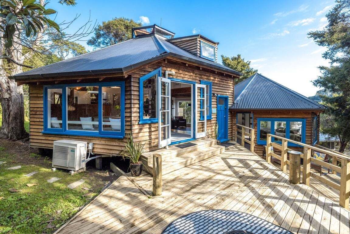 A wooden cabin with a deck, large windows, and a small attached structure.