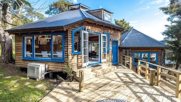 A wooden cabin with a deck, large windows, and a small attached structure.