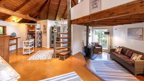 Un vaste espace de vie doté d’un haut plafond en bois, d’un escalier, d’un canapé et offrant une vue sur l’extérieur.