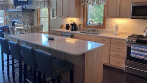 A modern kitchen with a central island, bar stools, a stone fireplace, wooden cabinets, and a large window. - Lakefront home with private dock on Lake Ossipee in Freedom, NH sleeps up to 10 (Freedom)
