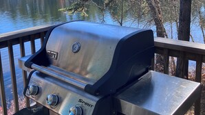 A Weber Spirit grill on a wooden deck overlooking a lake with trees. - Lakefront home with private dock on Lake Ossipee in Freedom, NH sleeps up to 10 (Freedom)