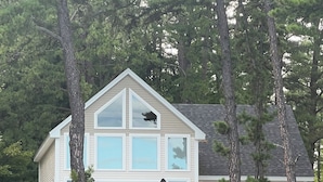 A two-story house with a balcony, a dock extending into a body of water, and a yellow kayak on the dock. - Lakefront home with private dock on Lake Ossipee in Freedom, NH sleeps up to 10 (Freedom)