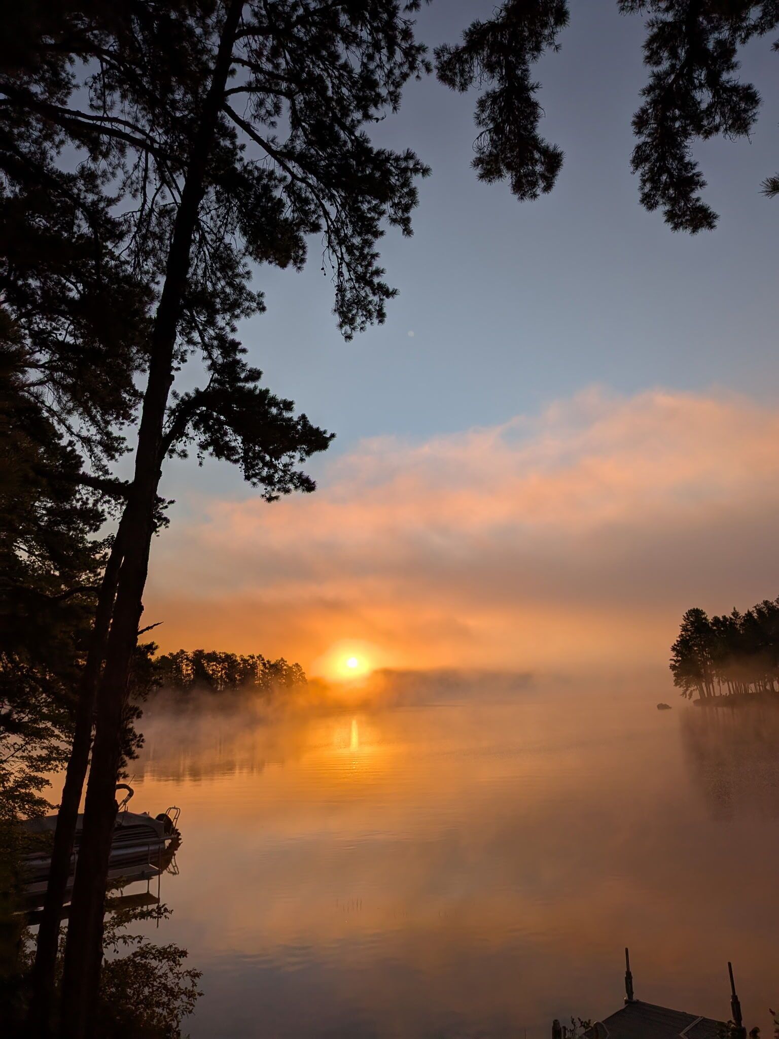 A serene lakeside view with a sunrise, trees, and a dock.