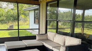 Zona d'estar exterior coberta amb un sofà modular i dos poufs, grans finestres i un paviment de pedra.
