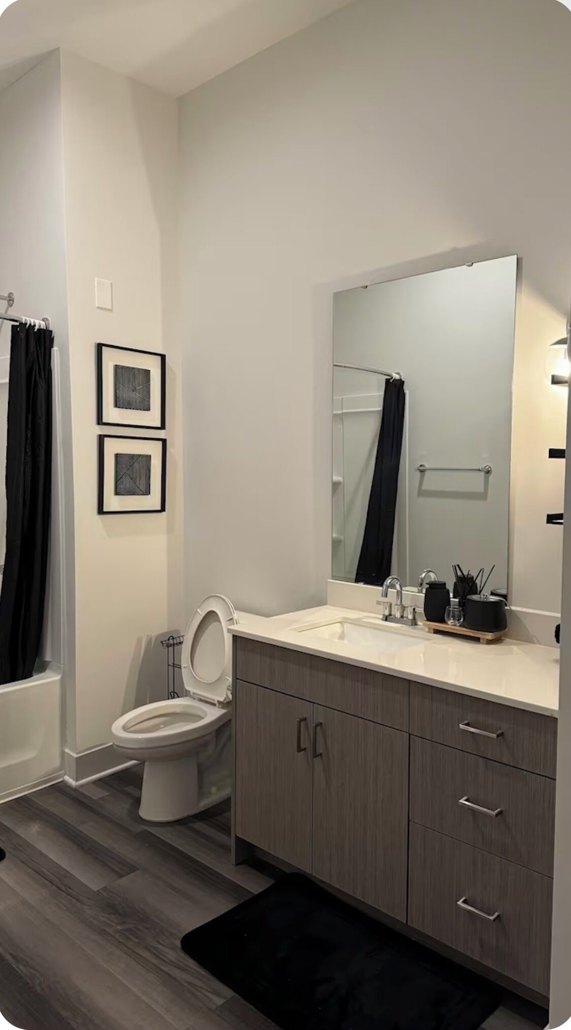 A modern bathroom with a toilet, sink, and vanity. There are two framed pictures on the wall, a shower curtain, and a mirror above the sink.