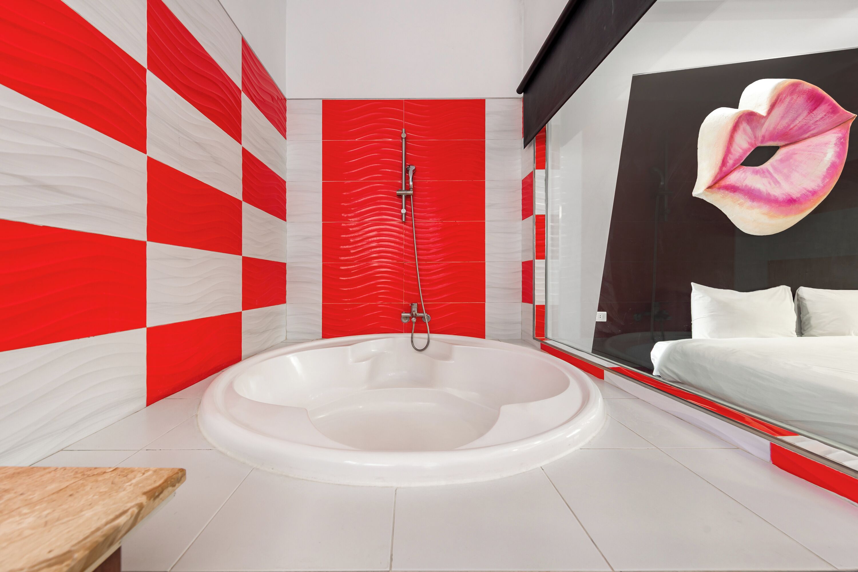 Ein modernes Badezimmer mit einer großen Badewanne, einer Duschkabine aus Glas und einem großen Spiegel, der ein Bett mit einem Zierkissen reflektiert.