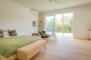 Un dormitorio amplio con una cama grande, un banco de mimbre, una silla y una pequeña mesa.