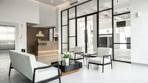 A modern reception area with a reception desk labeled "ASSA," two sofas, a coffee table, and a large window offering a view of the interior. - ASSA Hotel Semarang (Semarang)